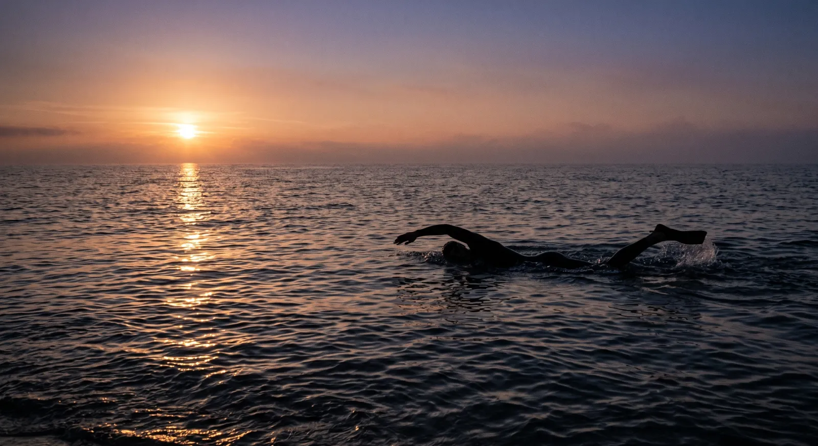 Silhouette of a swimmer performing the combat sidestroke in open ocean at dawn